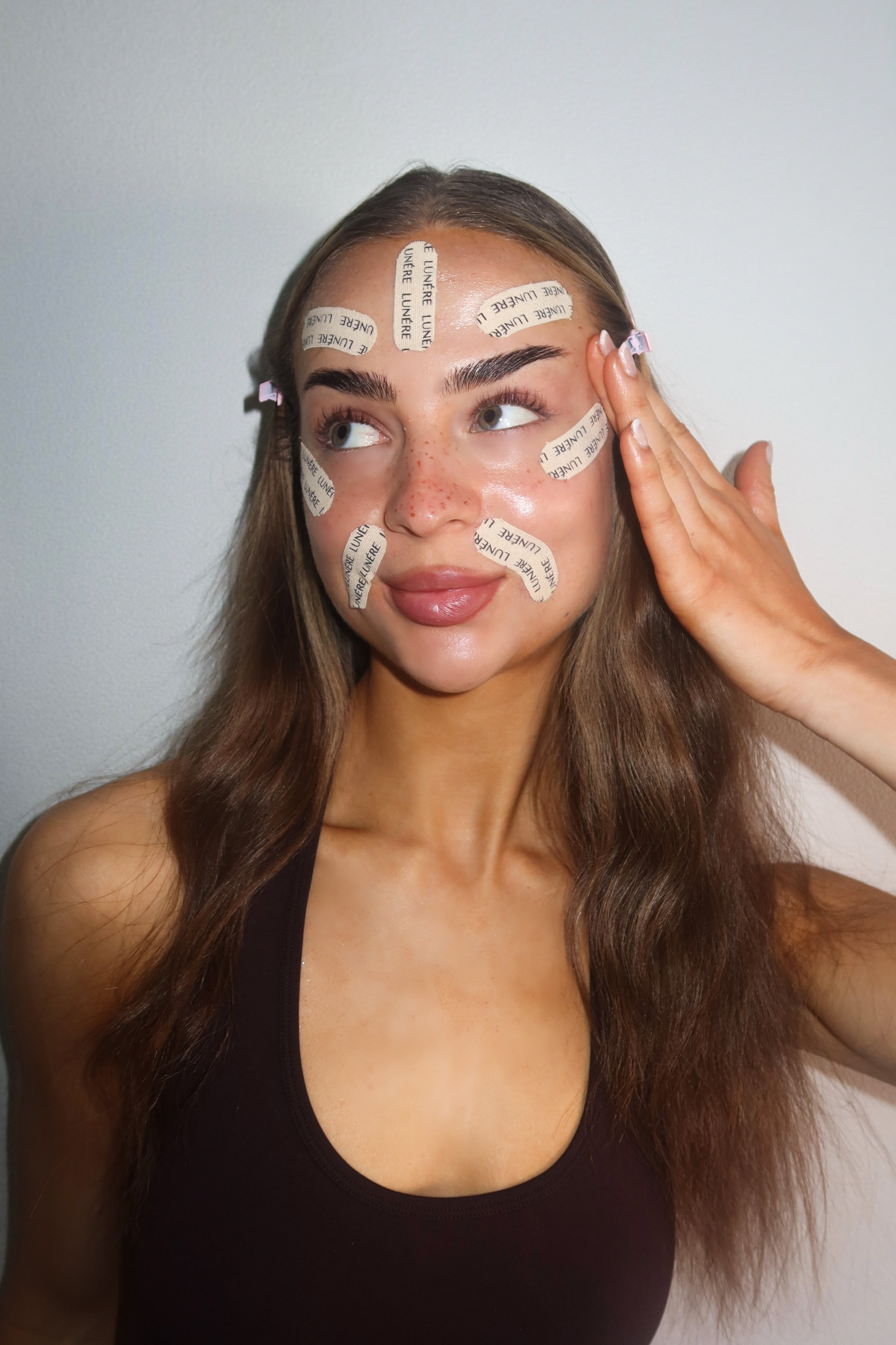 A young woman applying peptide-infused face tape on her forehead for smoother skin overnight.
